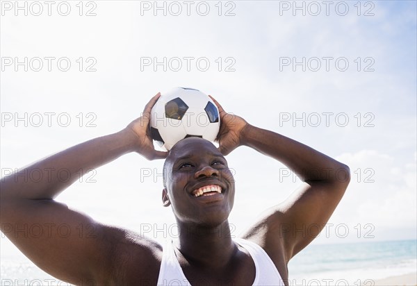 Mixed race man holding soccer ball on beach