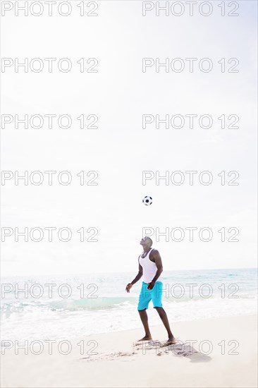 Mixed race man playing with soccer ball on beach