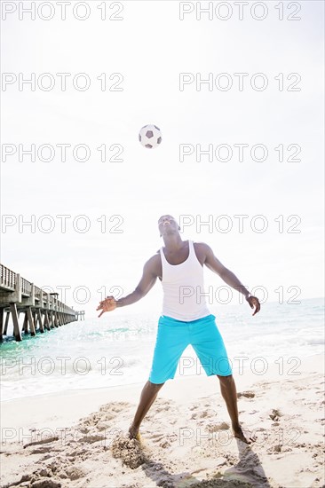 Mixed race man playing with soccer ball on beach