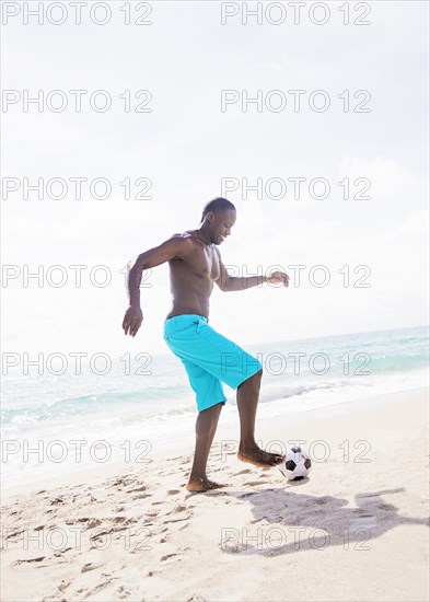 Mixed race man playing with soccer ball on beach