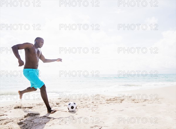 Mixed race man playing with soccer ball on beach