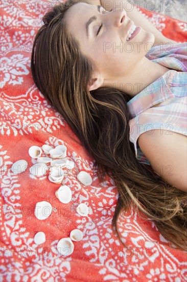 Smiling Caucasian woman laying on blanket with seashells