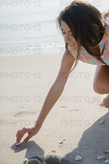 Caucasian woman collecting seashells on beach