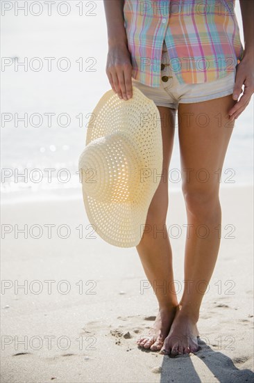 Caucasian woman holding sun hat on beach