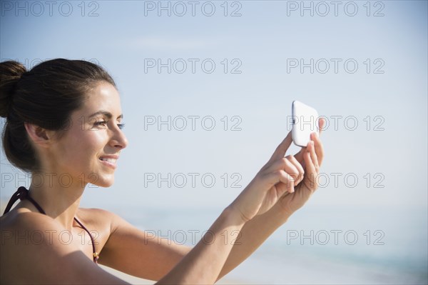 Caucasian woman taking selfie with cell phone at beach