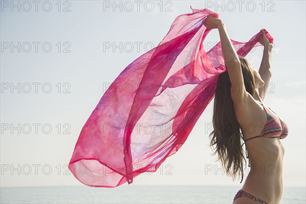 Caucasian woman holding fabric in wind at beach