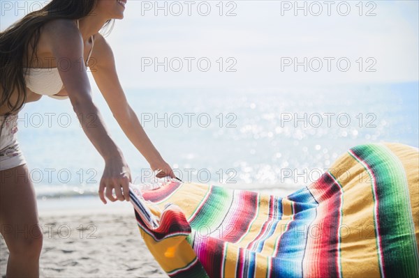 Caucasian woman spreading blanket on beach