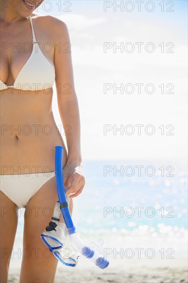 Caucasian woman holding snorkel and mask on beach