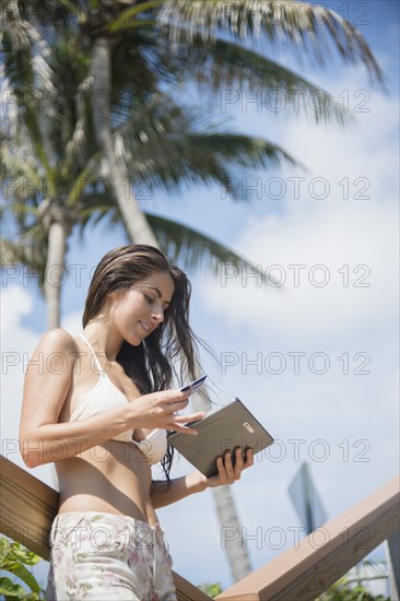 Caucasian woman shopping with digital tablet under palm tree