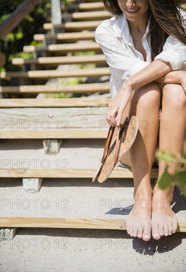 Caucasian woman with sandy feet sitting on beach staircase