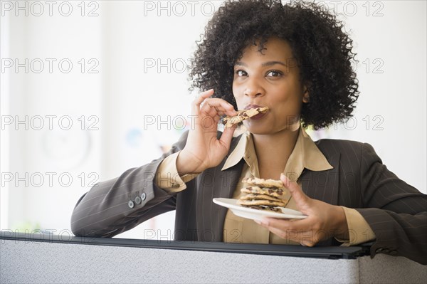 Businesswoman eating stack of cookies in cubicle