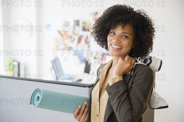 Businesswoman carrying yoga mat and sneakers in office