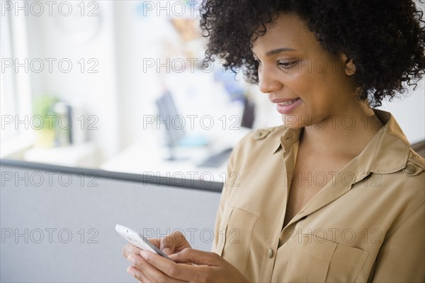 Businesswoman using cell phone in cubicle