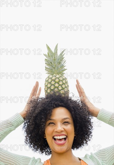 Smiling woman balancing pineapple on head