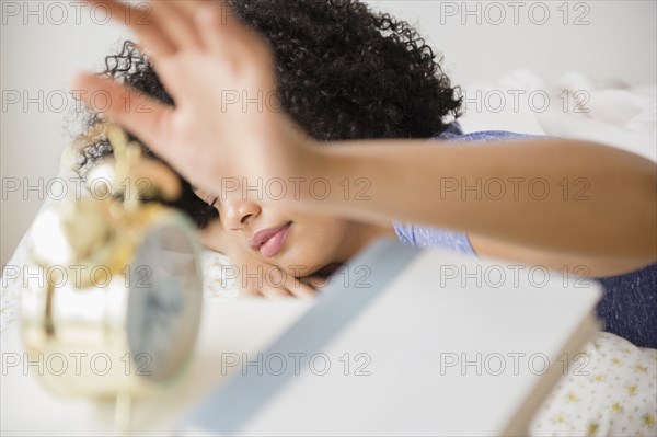 Woman turning off alarm clock in bedroom