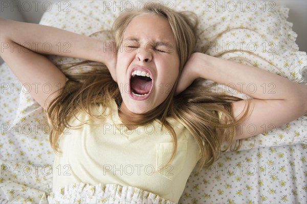 Shouting Caucasian girl covering her ears on bed