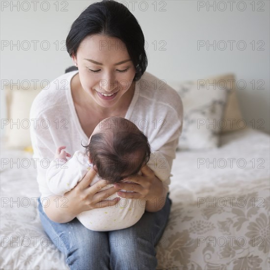 Asian mother holding baby on bed