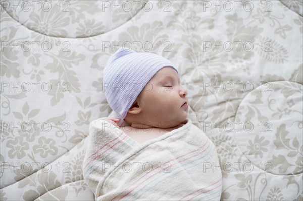 Swaddled Asian baby sleeping on bed