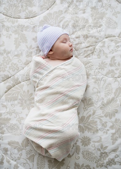 Swaddled Asian baby sleeping on bed