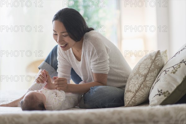 Asian mother playing with baby on bed