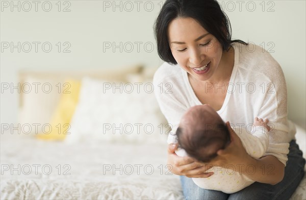 Asian mother holding baby on bed