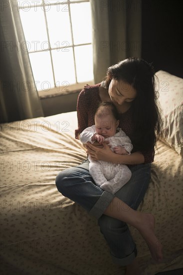 Asian mother holding baby on bed