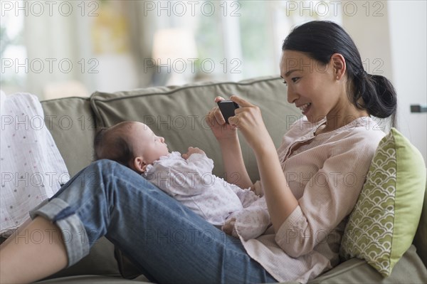 Asian mother taking cell phone photograph of baby in living room