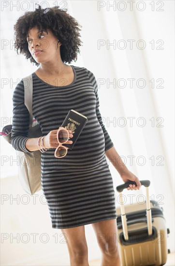 Pregnant African American mother pulling suitcase in airport