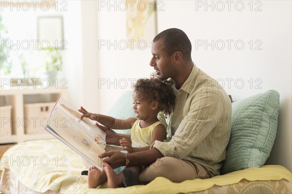 Father and daughter reading book on bed