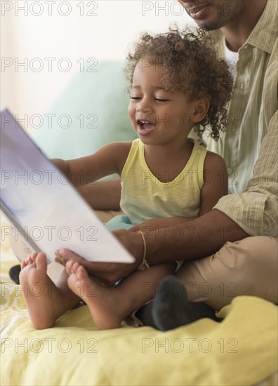 Father and daughter reading book on bed