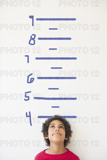 Mixed race boy measuring his height on wall chart