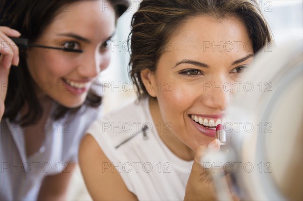 Hispanic women applying makeup in mirror