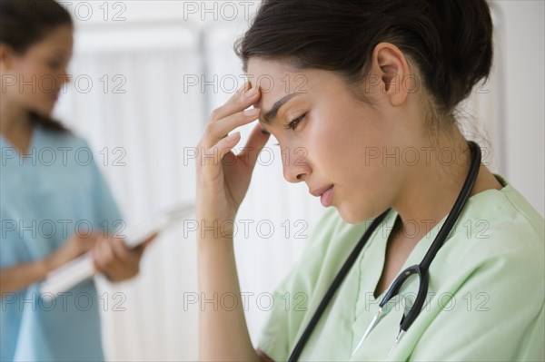 Hispanic nurse rubbing forehead at hospital