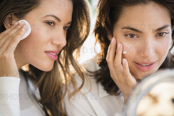 Hispanic women applying makeup in mirror