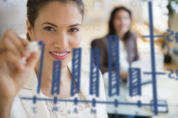 Hispanic businesswoman drawing chart on glass in office