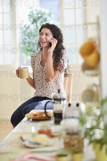 Mixed race woman talking on cell phone in kitchen