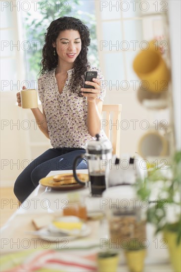 Mixed race woman using cell phone in kitchen