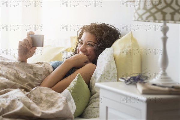 Mixed race woman using cell phone in bed