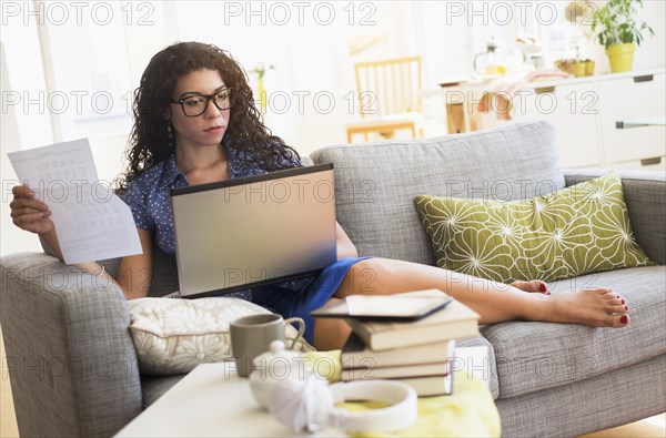 Mixed race woman paying bills on laptop on sofa