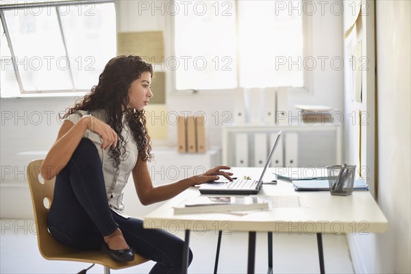 Mixed race businesswoman working on laptop at desk in office