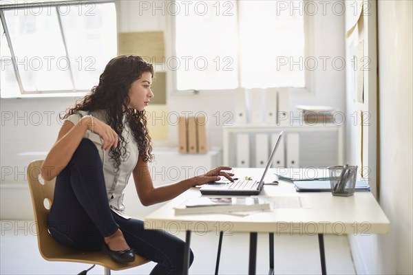 Mixed race businesswoman working on laptop at desk in office