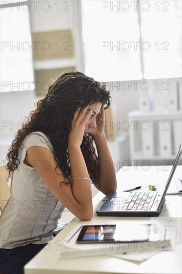 Frustrated mixed race businesswoman working on laptop at desk in office