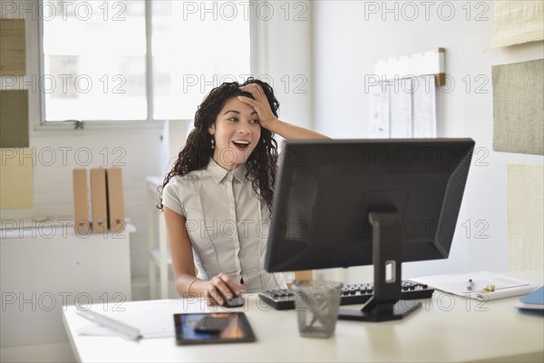 Mixed race businesswoman gasping at computer at desk in office