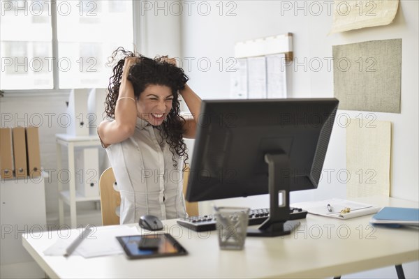 Mixed race businesswoman frustrated at computer at desk in office