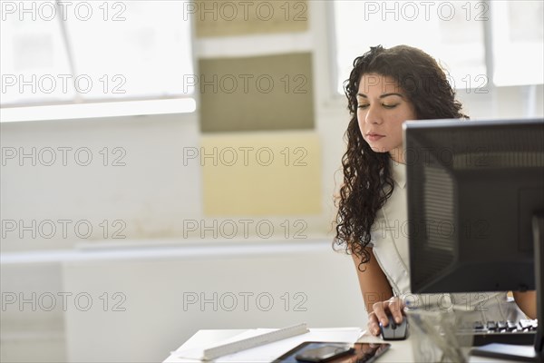 Mixed race businesswoman using cell phone and computer at desk in office