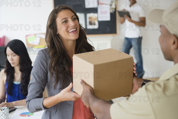Delivery man handing cardboard box to businesswoman in office