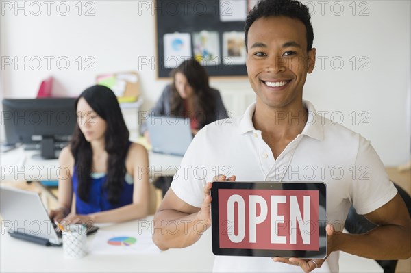 Businessman holding open sign on digital tablet in office