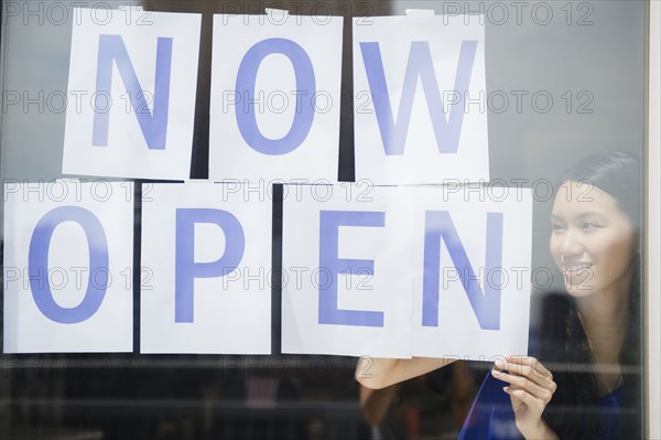 Woman hanging now open sign in store window