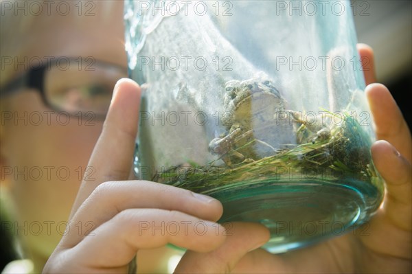 Close up of Caucasian boy holding jar with frog