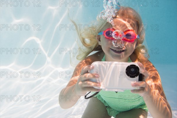 Caucasian girl taking photograph underwater in pool